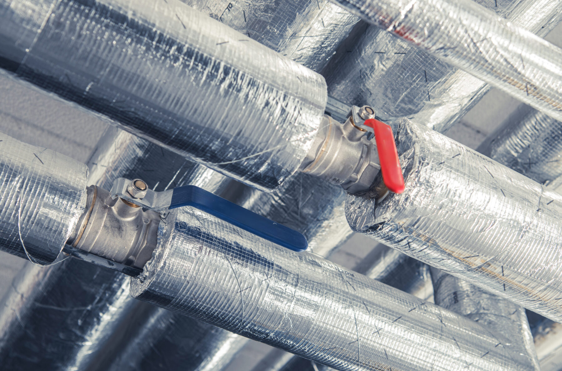Valve Controls On Insulated Metal Pipes In An Industrial Setting Under Bright Lighting